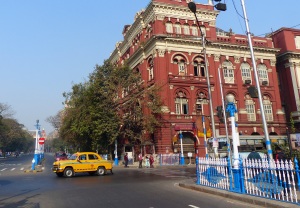 gelbes taxi der Marke Ambassador vor rotem alten Gebäude in Calcutta