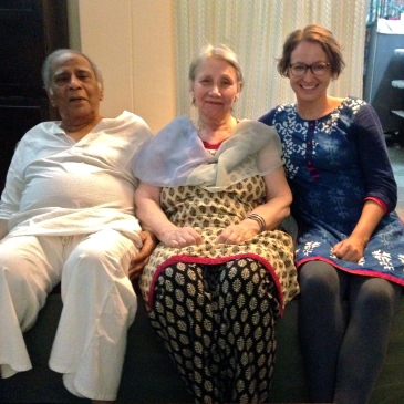 Älterer Mann in weißem Hemd sitzt mit seiner Frau und einer jüngeren Frau auf einem grünen Sofa